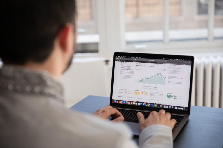 A professional business analyst reviewing data charts and financial analytics on a laptop screen at a desk.